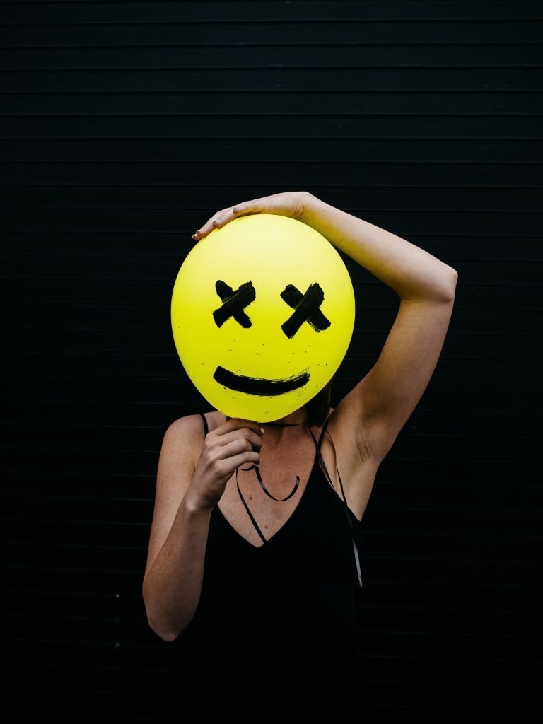 Image of a lady with a smiley face cut out in front of her face showing how I fake my chronic illness symptoms by painting on a smile