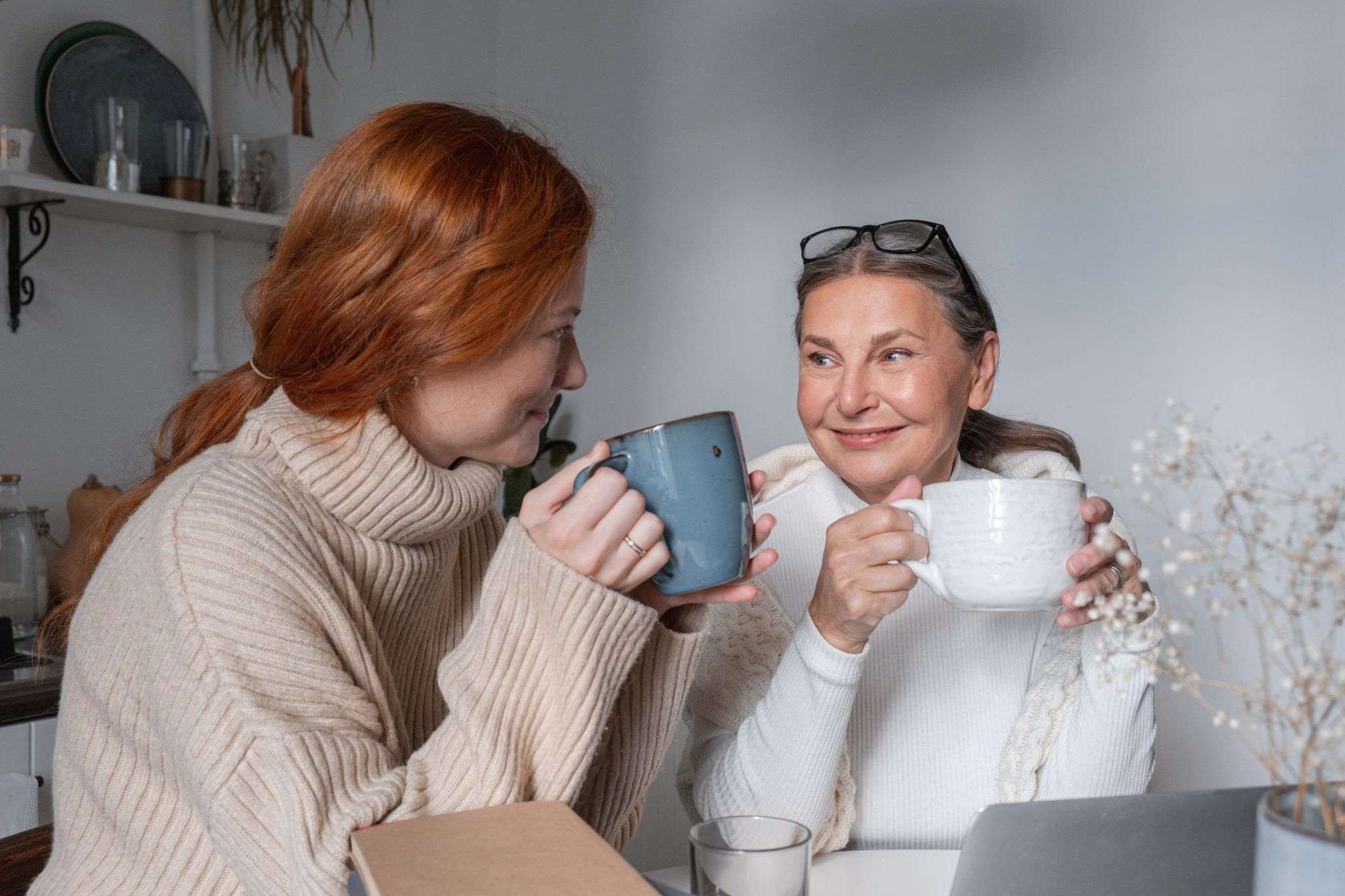 Two women enjoying a relaxing moment with coffee, sharing smiles and warmth indoors, supporting each other with perimenopause and chronic illness.